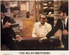 A USA lobby card featuring a scene from The Blues Brothers (1980). The scene includes Dan Ackroyd, Ray Charles and John Belushi